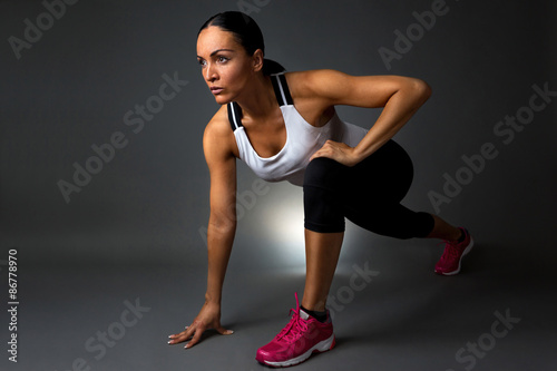 Attractive fitness woman preforming stretching exercise. Isolated against dark background.