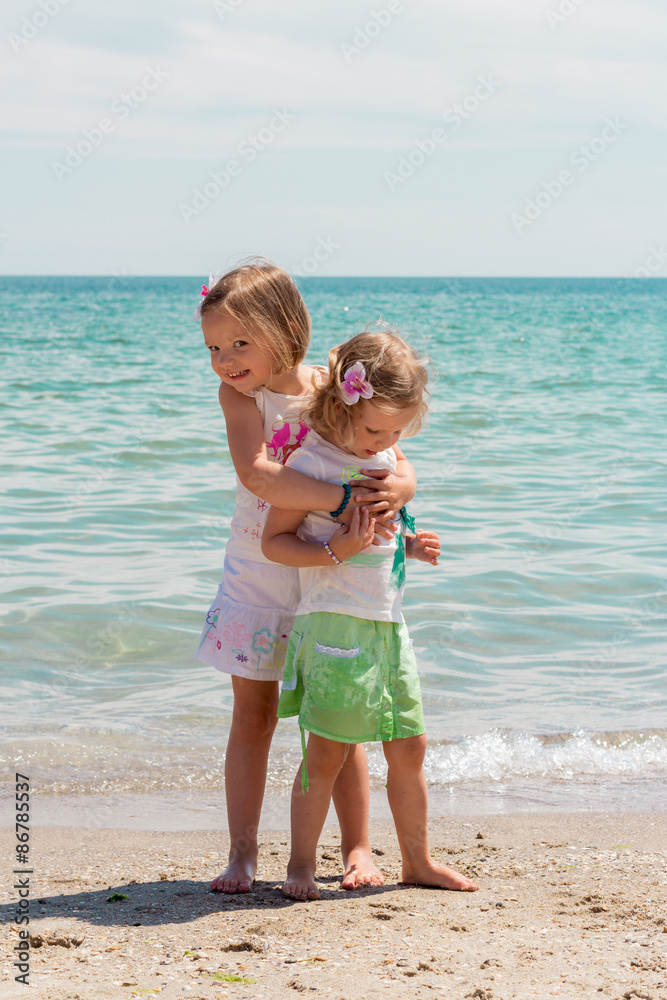 Beautiful little girls (sisters) play on the beach.