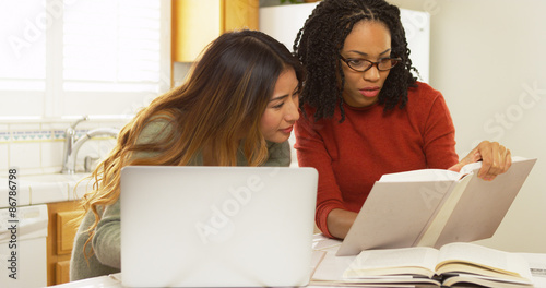 Two women students studying in kitchen with laptop computer