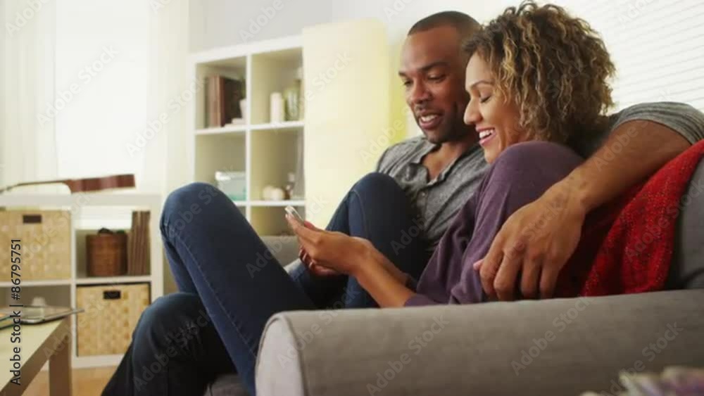 Black couple using smartphone together on couch Black couple using smartphone together on couch