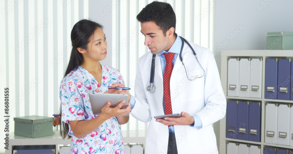 Fototapeta premium Mexican doctor talking with Asian nurse with tablets