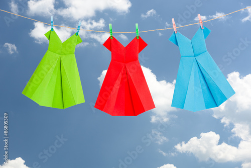 Three Origami paper dresses (green, red, blue) hanging on a clothes line in front of the blue summer sky