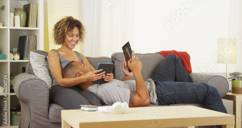 Black couple using their tablets on couch
