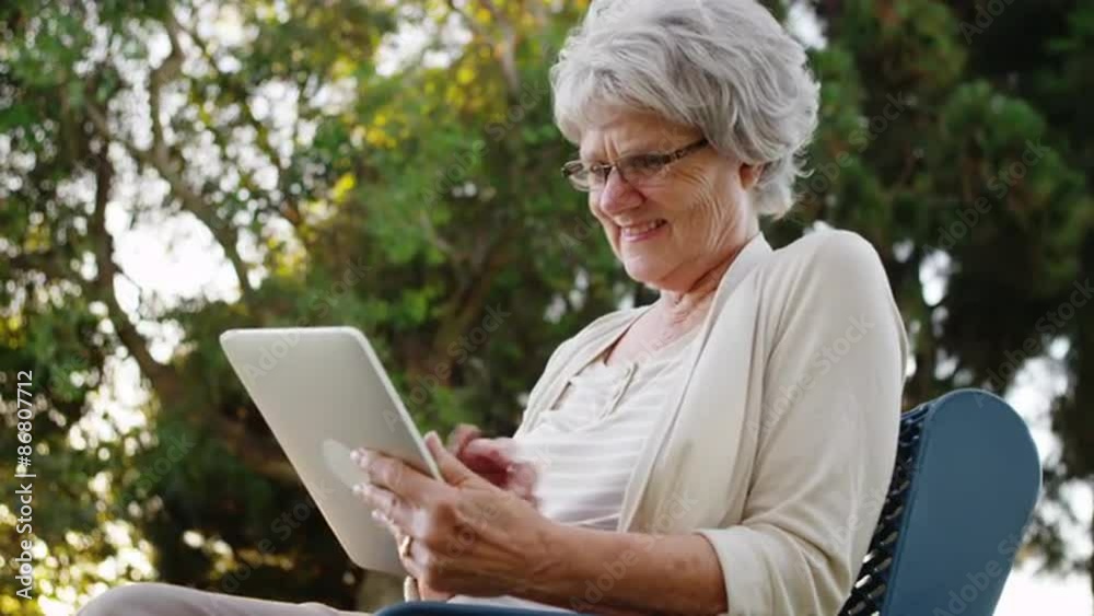 Happy senior woman using tablet at the park