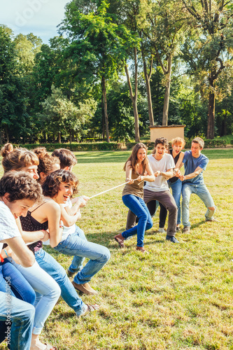 A group of ten teenage friends in a day of summer break from school, their fun at the park playing together tug of rope in a park