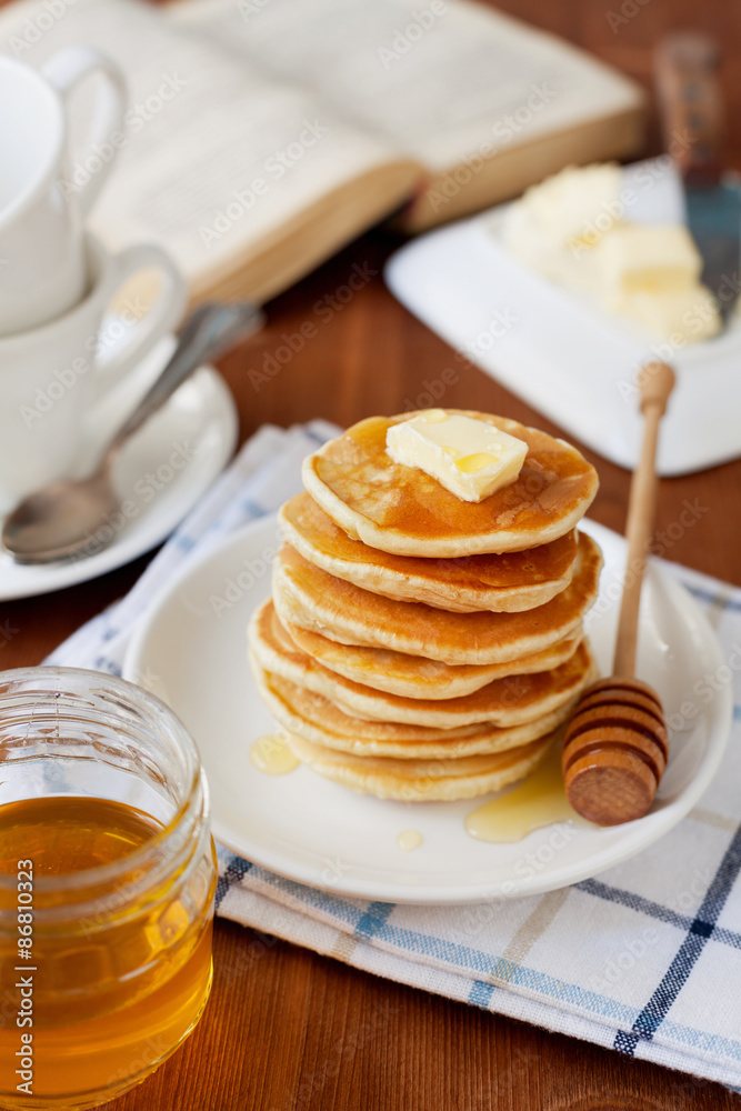 Stack of pancakes with honey syrup and butter in a white plate on a wooden rustic table with book, selective focus Stack of pancakes with honey syrup and butter in a white plate on a wooden rustic table with book, selective focus