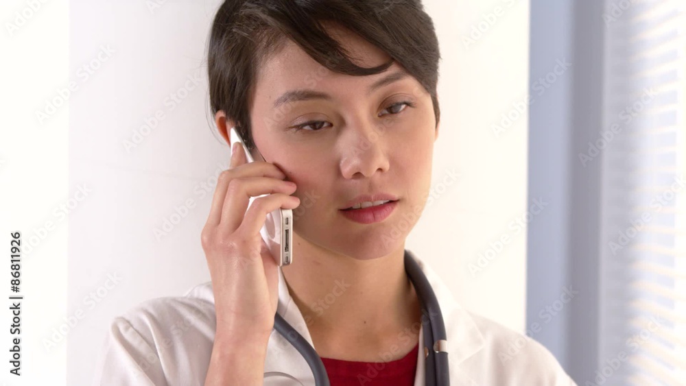 Attractive Asian doctor talking on smartphone Attractive Asian doctor talking on smartphone