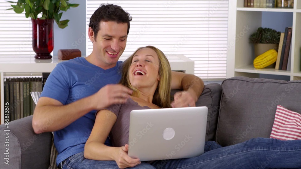 Couple laughing with laptop on couch Couple laughing with laptop on couch