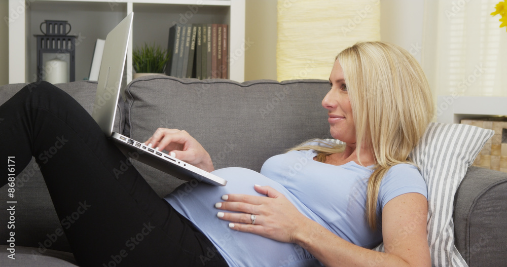 Happy pregnant woman lying on couch using laptop Happy pregnant woman lying on couch using laptop