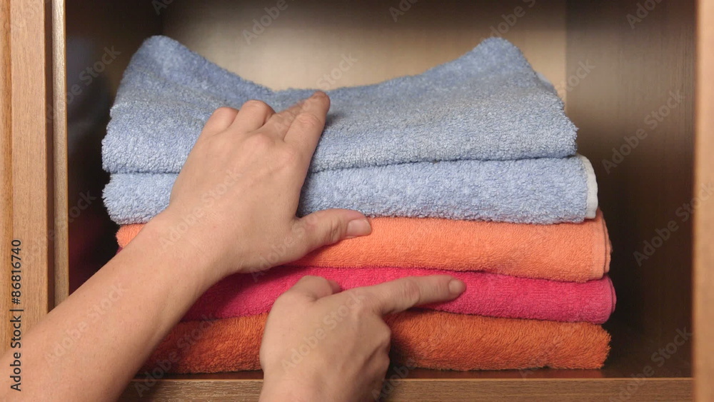 Female hands pulling out of the closet stack of colorful bath towels Female hands pulling out of the closet stack of colorful bath towels