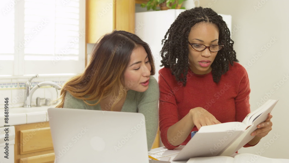Adult women college students reading book and using laptop computer to study Adult women college students reading book and using laptop computer to study