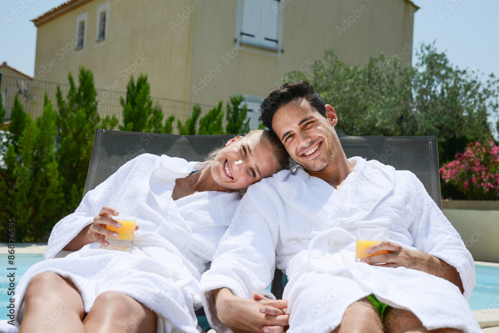 beautiful young couple resting in deck chairs with bathrobe by the pool of a thalasso resort - obrazy, fototapety, plakaty 