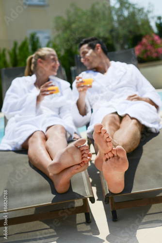 beautiful young couple resting in deck chairs with bathrobe by the pool of a thalasso resort