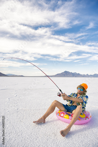 Redneck American fisherman wearing Hawaiian shirt goes on cheap ice fishing vacation holiday with inflatable pink ring in white desert
