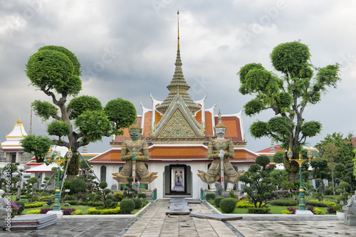 Grounds of Wat Arun in Bankgkok Thailand feature distinctive temple architecture with guardian figures and and decorative gardening