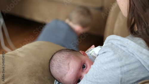 a mother nursing her baby boy while toddler plays photo