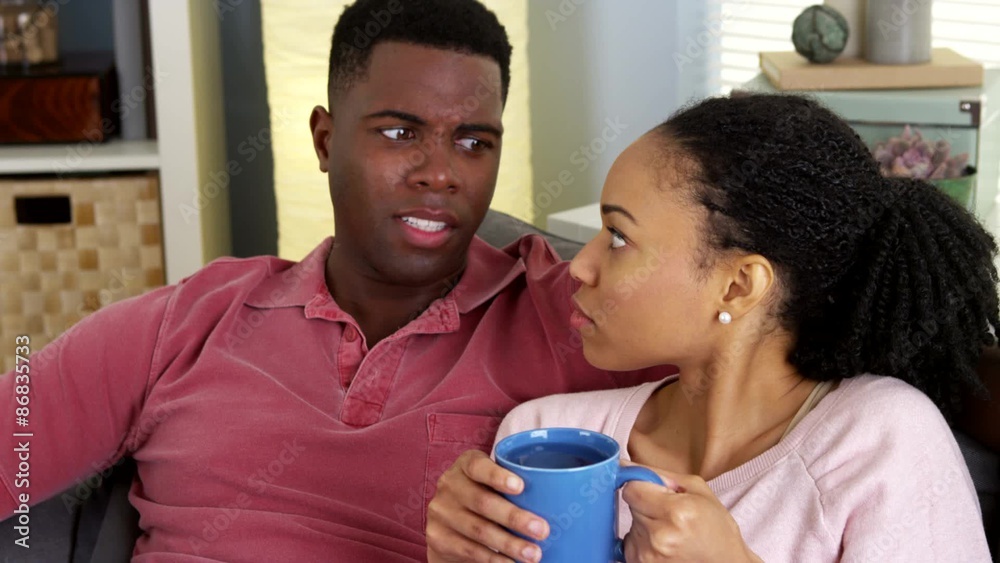 Young black couple sitting together on couch chatting Young black couple sitting together on couch chatting