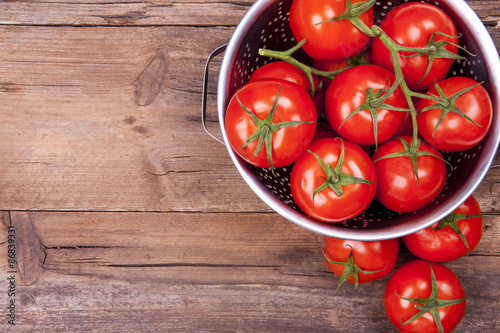 Bunch of tomatoes on vine in colander and out of it shot from above with negative space on a wooden background