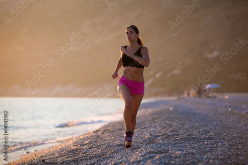 Runner woman jogging on beach in sports bra top.Beautiful fit female fitness woman training and working out outside in summer as part of healthy lifestyle.Fitness woman running at sunset on beach