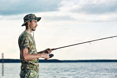 Young man in a camouflage fishing on the lake.