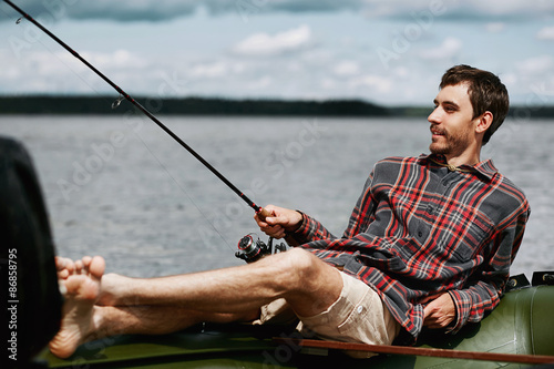 young happy man on vacation lying in the boat smile and fishing