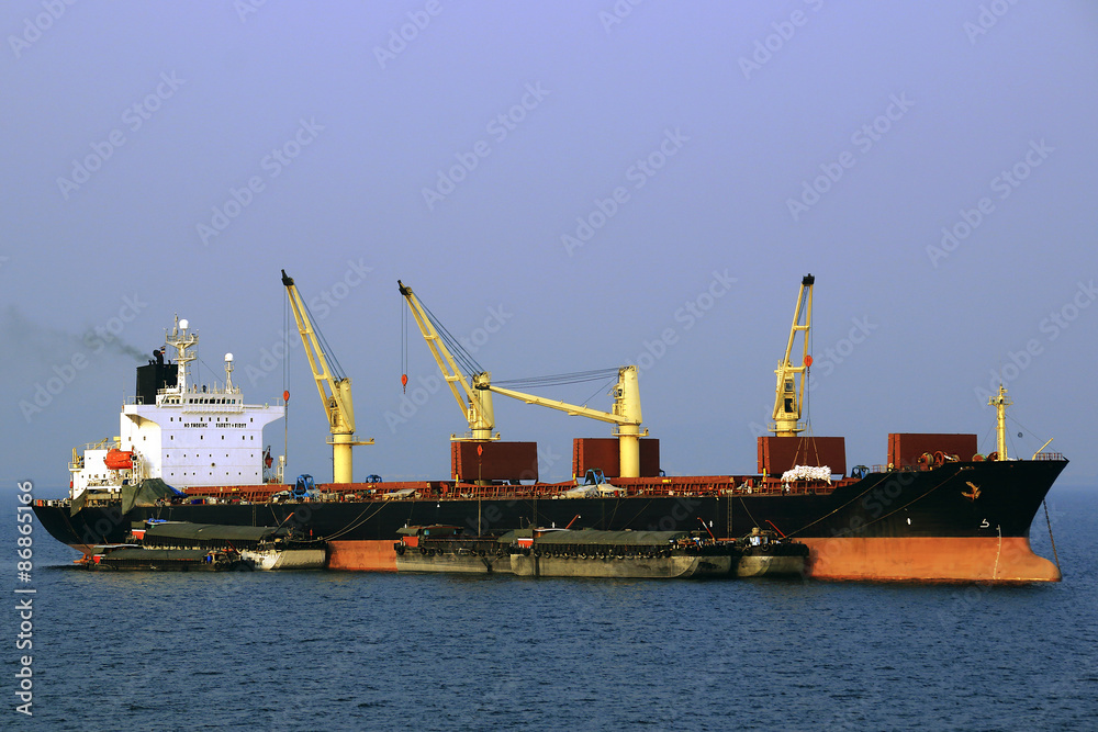 a large bulk carrier loaded with ship cranes work on the roads