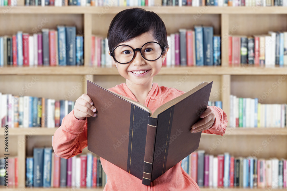Girl standing in library while reading textbook Girl standing in library while reading textbook