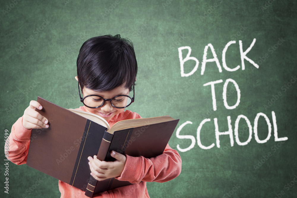 Fotografie Kid back to school and reading a book in class