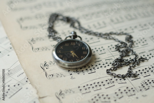 Old watch laying on old piano musical notes