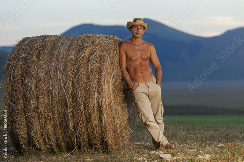 Cowboy a torso nudo su una balla di fieno. Montagne all'orizzonte photo