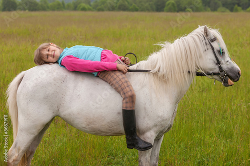 The little girl lay on her back white horse and smiling  Outdoors