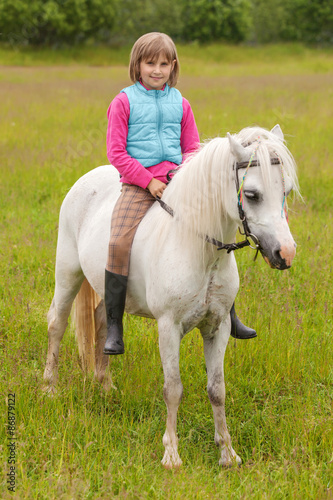 Young girl child sitting astride a white horse and smiling  Outdoors © andreipugach