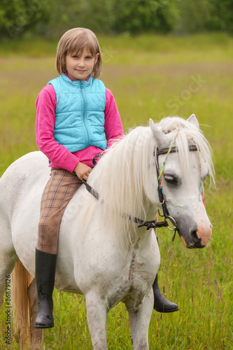 Young girl child sitting astride a white horse and smiling Outdoors