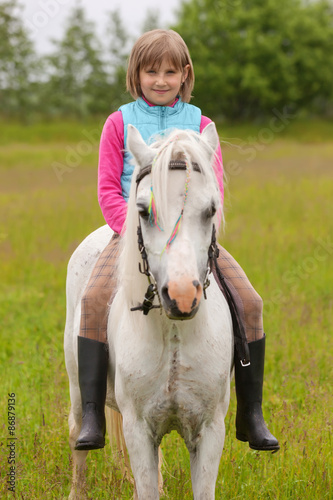 Young girl child sitting astride a white horse and smiling Outdoors