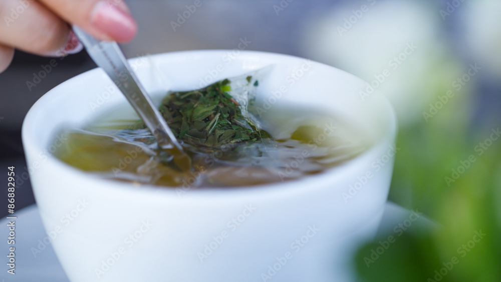 Female hand stirring a cup of herbal tea with a spoon Female hand stirring a cup of herbal tea with a spoon