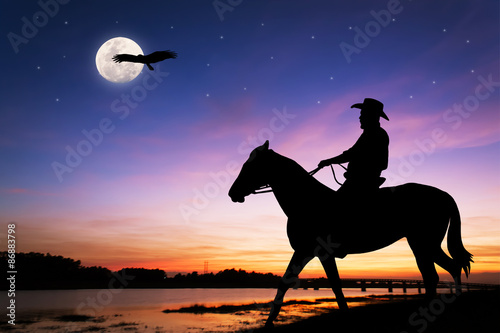 silhouette of Cowboy sitting on his horse at river full moon after sunset background