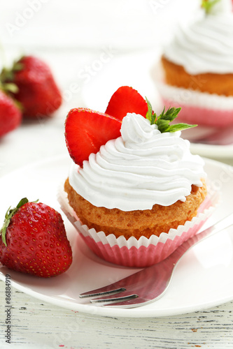 Tasty cupcake with strawberry on white wooden background