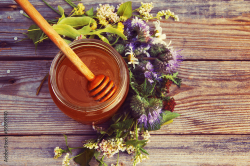 Honey in a glass jar with June flowers melliferous herbson a wooden surface. Honey with flowers photo