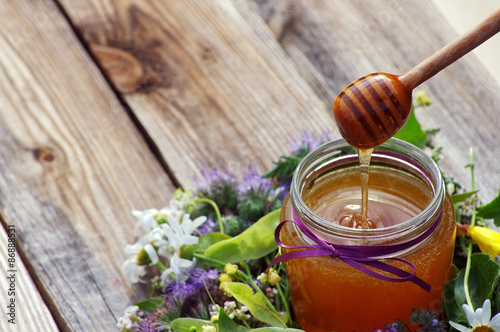 Honey in a glass jar the tied gift tape with a bow with June flowers melliferous herbson a wooden surface. Honey with flowers photo