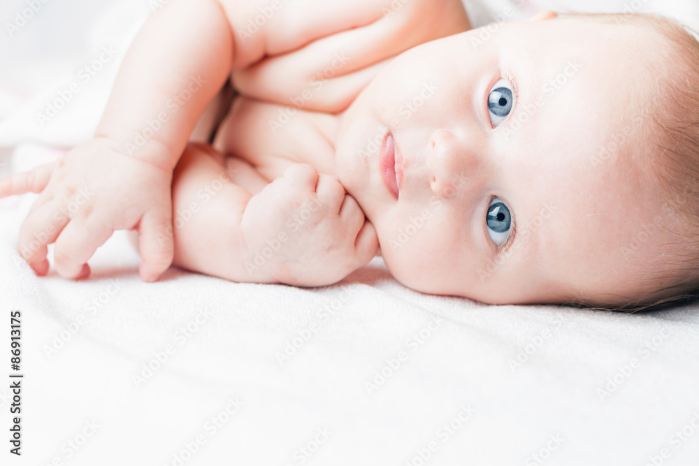 Newborn baby with beautiful eyes lying on a white bed or background and looking at camera, with large copy space for any text. Concept of baby care