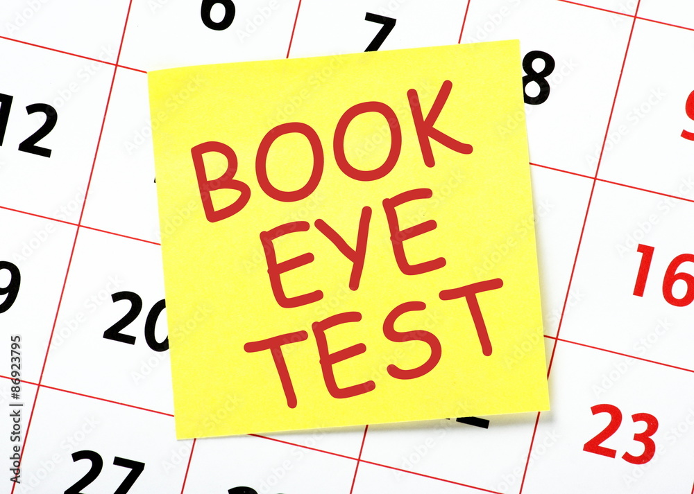 A yellow sticky note reminder to book an eye test posted on the page of a calendar A yellow sticky note reminder to book an eye test posted on the page of a calendar