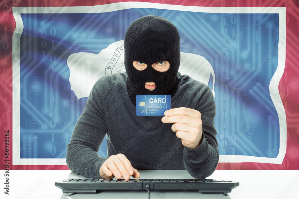 Hacker holding credit card and USA state flag on background - Wyoming Hacker holding credit card and USA state flag on background - Wyoming