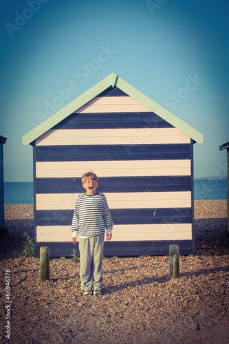 CHILD WITH A STRIPED JUMPER NEXT TO A STRIPED BEACH HUT