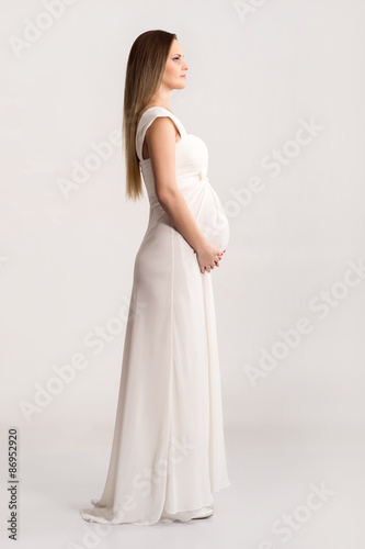 Young and beautiful pregnant woman in antique dress over grey background with a lot of blank space
