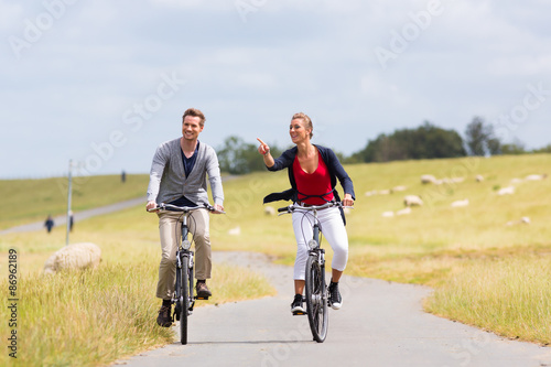 Paar, Mann und Frau, bei Radtour mit dem Fahrrad am Deich mit Schafen