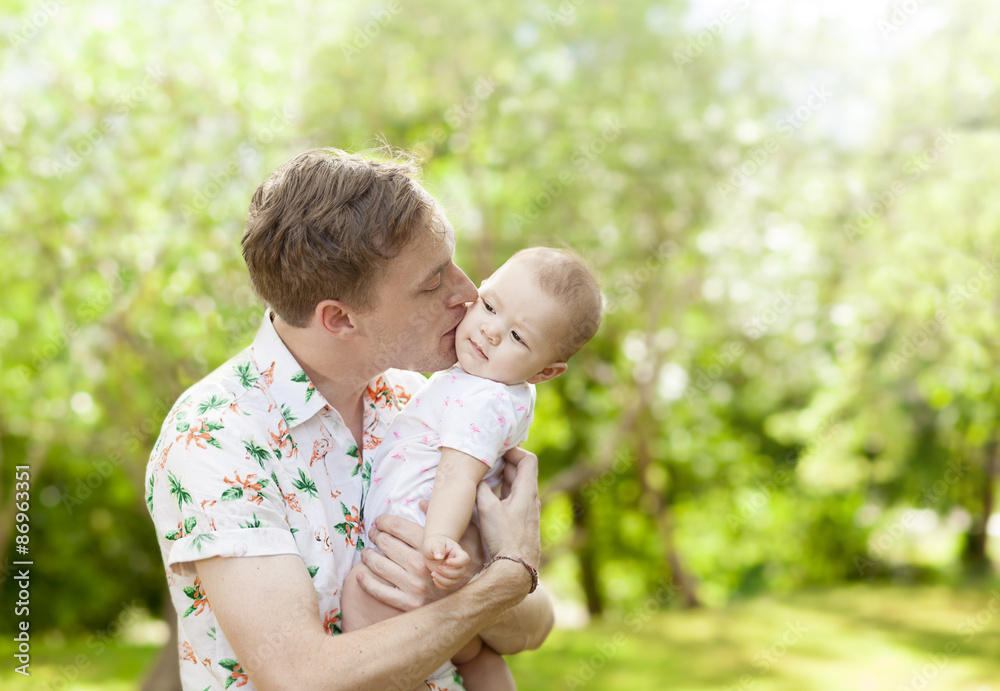 Father kissing his cute baby outdoors in spring park against na Father kissing his cute baby outdoors in spring park against na
