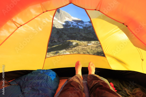 Man lying with bare feet in tent with a view at the mountains.