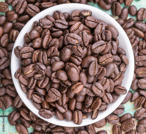 Roasted coffee beans in white bowl over rustic wooden background