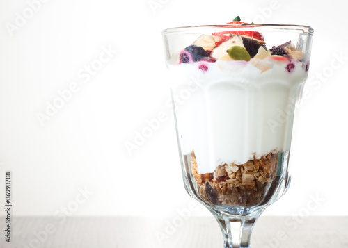 Homemade granola with Greek yoghurt topped with frozen berries, coconut and a fresh strawberry.Served in a tall glass.