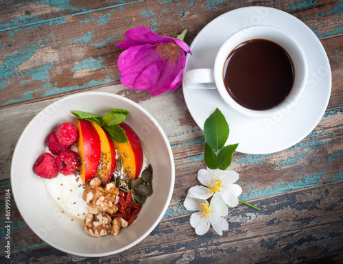 A bowl of healthy breakfast muesli with yogurt and topped with fresh blackberries, sliced nectarine, goji berries, pumpkin seeds and walnuts.Served with fresh coffee and wild flowers.